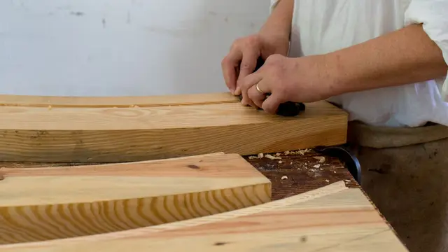 Un artisan rabote une planche de bois sur son établi